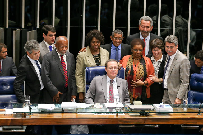 Imagem mostra parlamentares de diferentes cores de pé em frente 'a mesa de madeira do senado