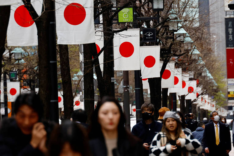 Pessoas passam pelas bandeiras nacionais do Japão em um bairro comercial em Tóquio, Japão, em 19 de março de 2024