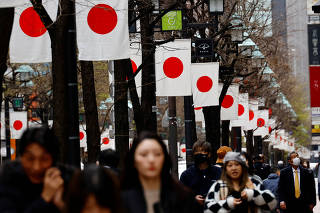 People walk past Japan?s national flags in a shopping district in Tokyo