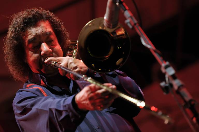 Em foto colorida, o trombonista, saxofonista, compositor e arranjador Raul de Souza aparece tocando um trombone