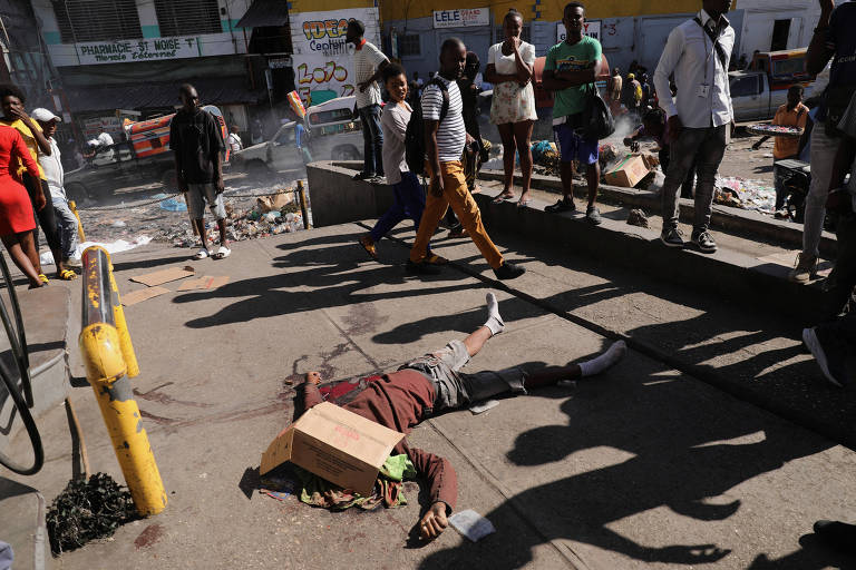 Pessoas caminham ao lado de homem morto a tiros na capital do Haiti, Porto Príncipe