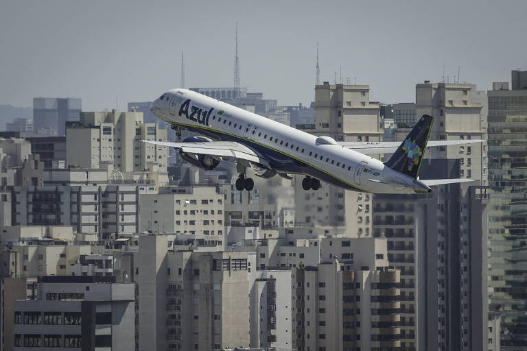 Avião no ar depois de decolagem. Ao fundo, é possível ver dezenas de prédios em São Paulo.