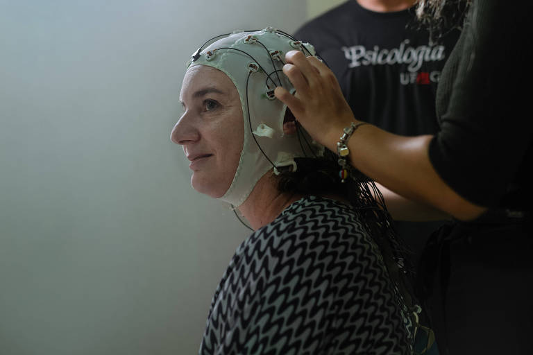 Uma mulher veste uma touca de pano repleta de eletrodos para medição da atividade cerebral. Ele está em uma sala de paredes brancas na Universidade Federal de Minas Gerais