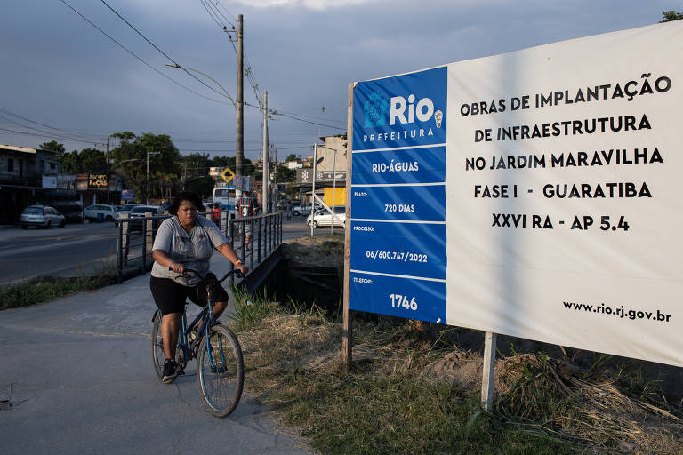 Moradora passa próxima a obra de infraestrutura no bairro Jardim Maravilha, em Guaratiba, zona oeste do Rio de Janeiro