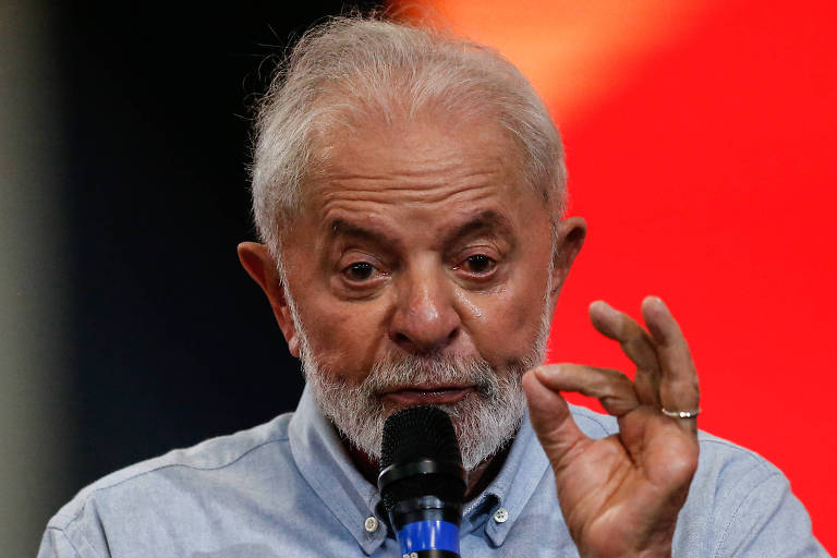 Lula está falando ao microfone e está com uma das mãos levantada