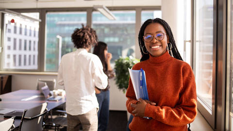 Black girl in office in foreground is looking at camera - (Photo: Jessica/Adobe Stock) DIREITOS RESERVADOS. NÃO PUBLICAR SEM AUTORIZAÇÃO DO DETENTOR DOS DIREITOS AUTORAIS E DE IMAGEM