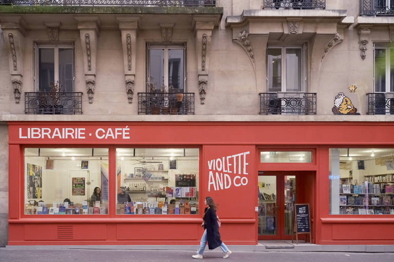 Pessoa caminha em frebte a fachada vermelha, com sacadas de prédios com flores, em Paris