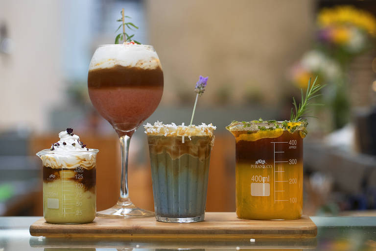 Quatro copos com bebidas coloridas: uma verde com marrom; outra rosa com marrom; outra azul com marrom; e outra laranja com marrom