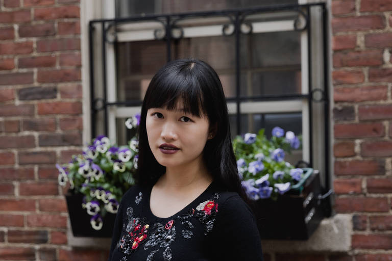 mulher asiática jovem com as mãos cruzadas e vestido preto com detalhes de flores vermelhas