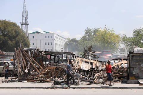 People walk past remains of vehicles near the presidential palace, after they were set on fire by gangs, as violence spreads and armed gangs expand their control over the capital, in Port-au-Prince, Haiti March 25, 2024. REUTERS/Ralph Tedy Erol ORG XMIT: GGGHNR09