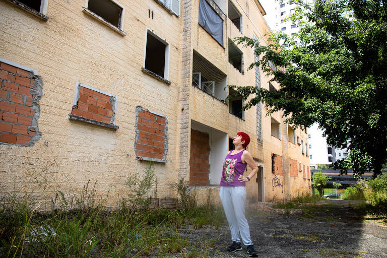 Mulher olha prédio com sinais de abandono e vandalismo