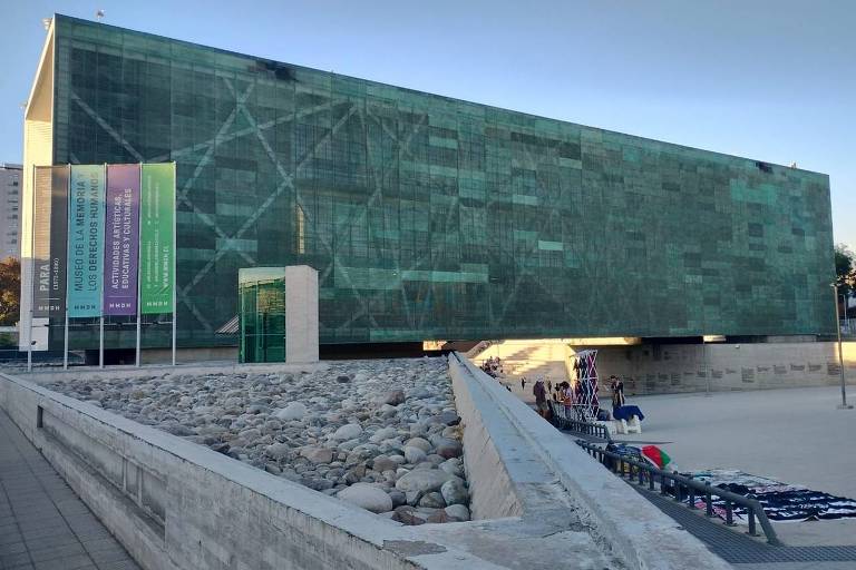 Foto tirada do pátio de um prédio retangular e verde, com faixas na entrada