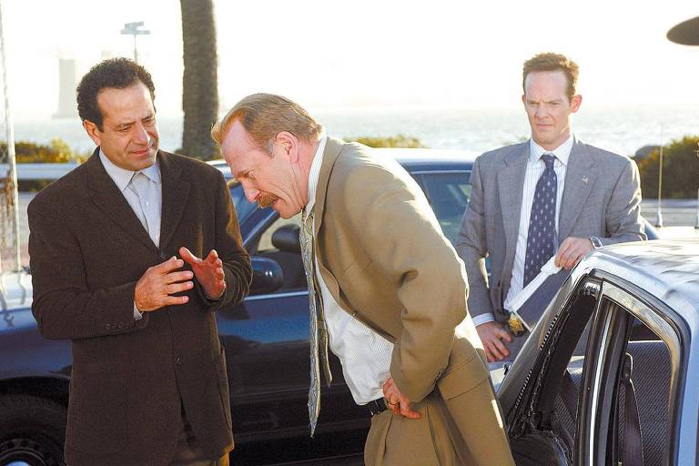 Três homens conversam junto a um carro. Um deles, Monk, à esquerda, explica algo ao homem à direita, que parece bravo. Atrás dos dois, um terceiro homem acompanha a conversa
