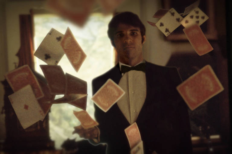 Um jovem Steve Martin, vestindo um smoking, em meio a cartas de um baralho que voam pelo ar