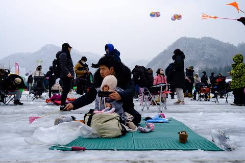 A man holds a phone for his baby as he fishes for trout through a hole on a frozen river during the annual ice fishing festival in Hwacheon, some 120 kilometers northeast of Seoul, on January 7, 2023. (Photo by ANTHONY WALLACE / AFP)