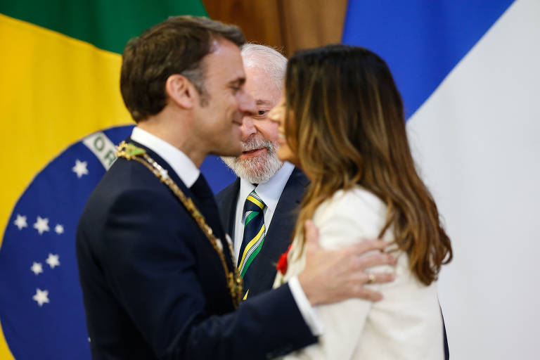 O presidente da França, Emmanuel Macron, cumprimenta a primeira-dama Janja da Silva diante de Lula no Palacio do Planalto