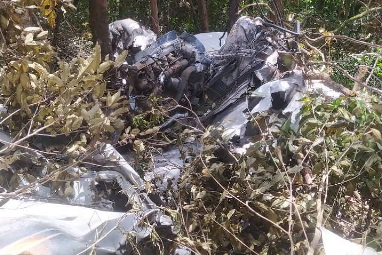 destroços de aeronave em mata, com partes de metal retorcido em meio a galhos e vegetação