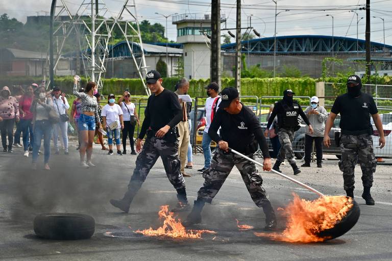 Policiais com roupas camufladas tentam conter fogo em pneus durante uma rebelião em um presídio