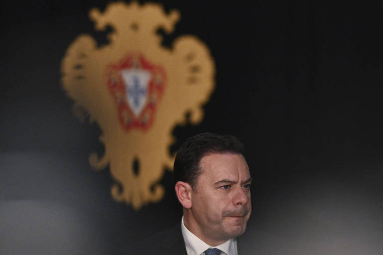 Imagem mostra um close no rosto do social-democrata Luís Montenegro, que assume o posto de primeiro-ministro de Portugal na terça-feira (2). Ele é um homem branco e está vestido com um terno, podemos ver o colarinho de sua camisa branca e parte da gravata. Ele está em frente a um brasão de Portugal