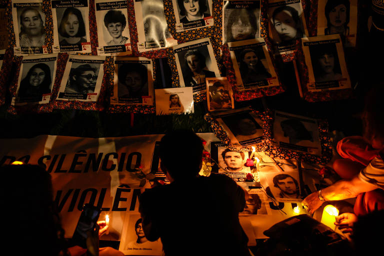 imagem geral mostra silhueta de pessoas em meio a fotos, velas e flores durante manifestação em homenagem às vítimas do golpe militar de 1964.