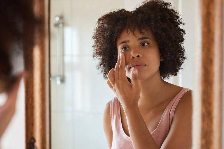 Mulher negra passando cosmético em frente a um espelho