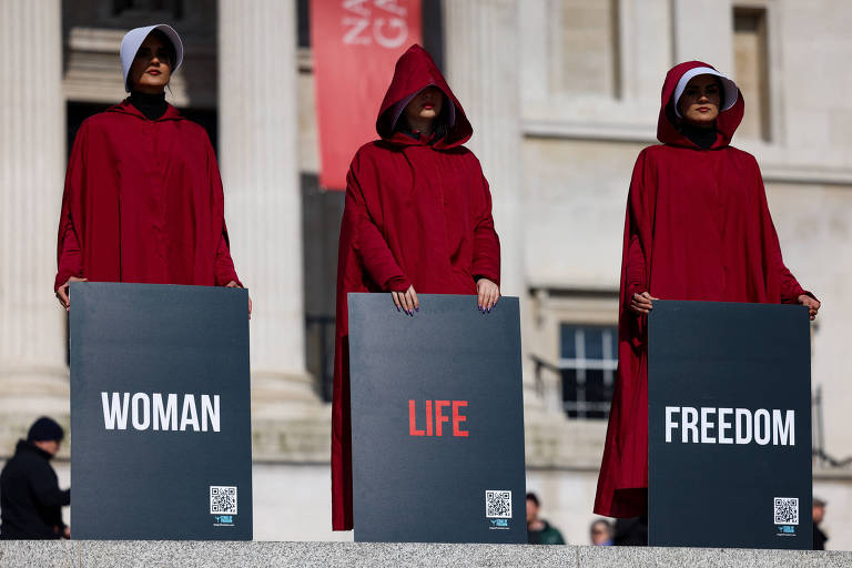 Mulheres com roupas vermelhas e placas com os dizeres: woman (mulher), life (vida) e freedom (liberdade)