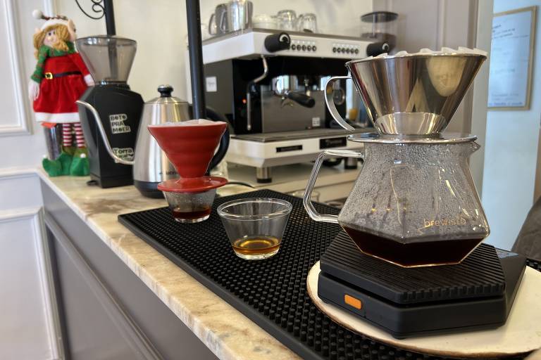 Café sendo coado em jarra de vidro com máquina de café espresso ao fundo