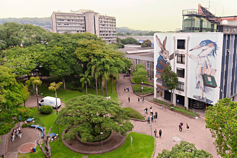 Vista aérea de campus da PUCRS. Há árvores e fachadas de prédios e alguns alunos em circulação