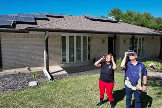 Eclipse chaser Leticia Ferrer and her husband Daniel Brookshier observe the sun through eclipse glasses, in front of their home in Dallas