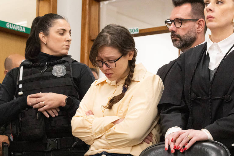 No centro da imagem, uma mulher branca de trança e óculos, está cabisbaixa e rodeada pora agentes da lei