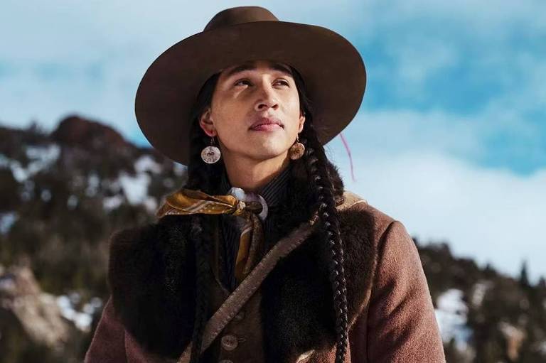 Cole é um homem indígena norte-americano. Ele usa tranças e um chapéu.