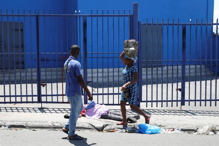 Mulher e homem caminham em rua da capital Porto Príncipe ao lado de corpo apenas coberto por um tecido