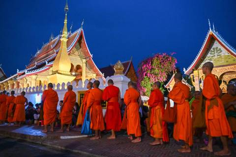 (FILES) Buddhist monks line up at dawn to receive food and alms from devotees in front of a pagoda in Luang Prabang on January 28, 2024. As dawn broke over Luang Prabang, saffron-robed monks trod the streets receiving alms -- but a cacophonous influx of camera-clutching tourists shattered the peace of the ancient Laotian town. (Photo by TANG CHHIN SOTHY / AFP)
