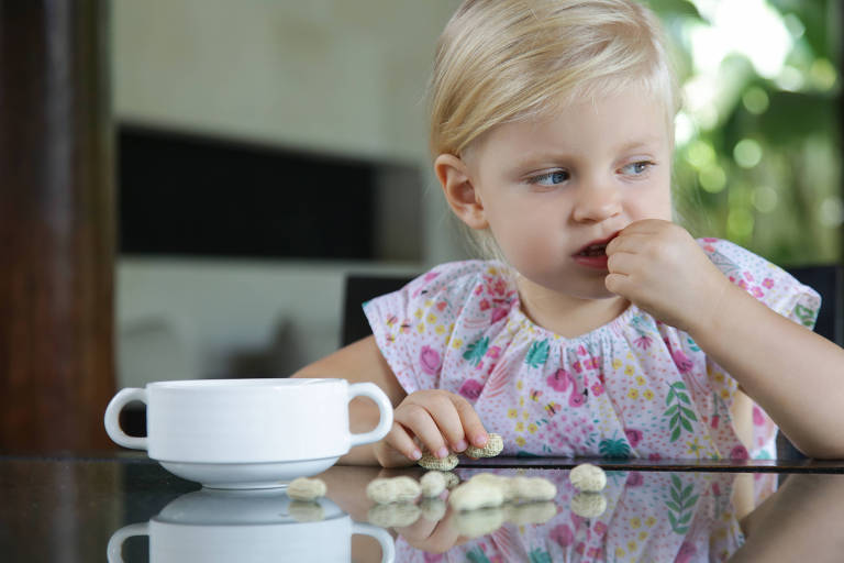 Menina criança comendo amendoim com casca na mesa da cozinha