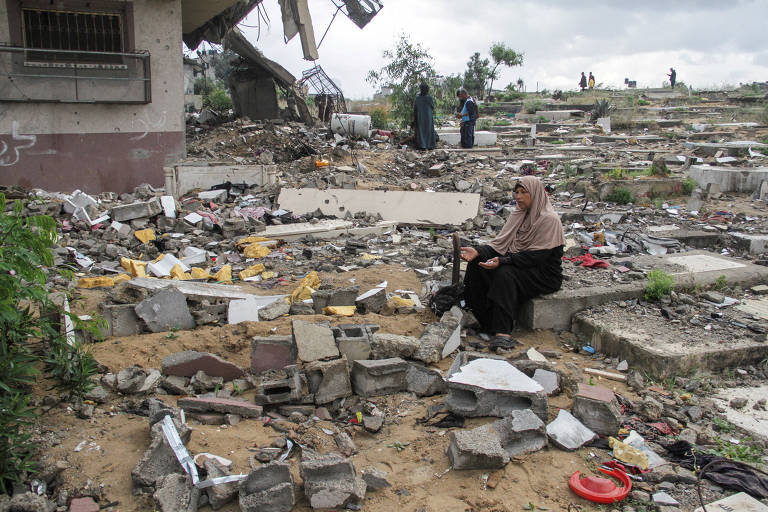 Mulher palestina senta em meio a destroços na Faixa de Gaza