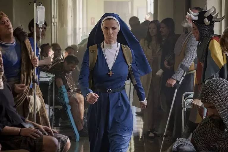 Uma mulher vestida de freira caminha obstinadamente por um corredor de hospital lotado de homens fantasiados de cavaleiros medievais, todos feridos e cansados
