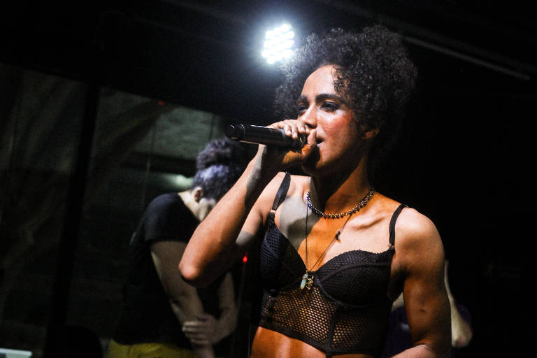 A imagem mostra uma mulher vestida de preto e com microfone na mão