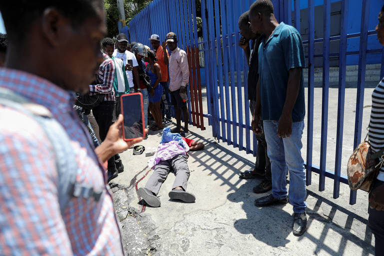 Pessoas olham e tiram fotos de corpo de homem morto após confronto entre gangues em Porto Príncipe