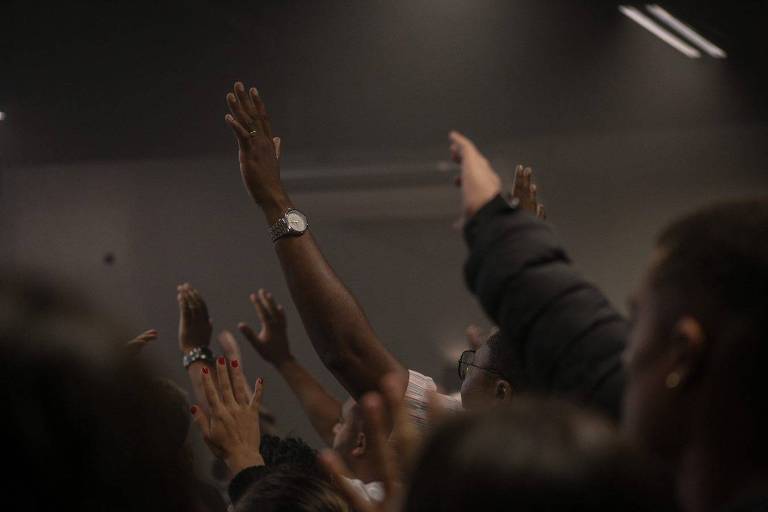 Foto de diversas pessoas orando com as mãos erguidas 