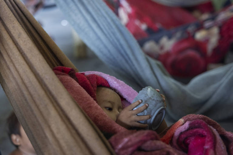 Criança yanomami com desnutrição grave se alimenta deitada em rede