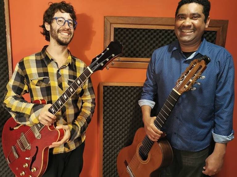 Em foto colorida, o guitarrista Tom Cykman e o violonista Félix Júnior posam sorrindo para a câmera