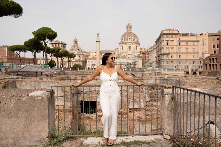 Mulher branca de roupas brancas posa em frente à paisagem histórica de Roma