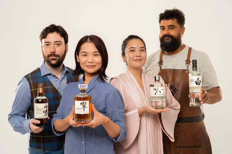 A foto mostra quatro pessoas, sendo dois homens e duas mulheres, que seguram garrafas de destilados da empresa Suntory