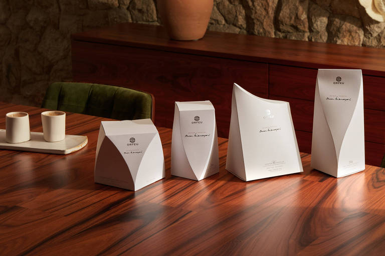 A foto mostra quatro embalagens de café em papel rígido branco com formas de contornos curvilíneos inspiradas na obra de Oscar Niemeyer