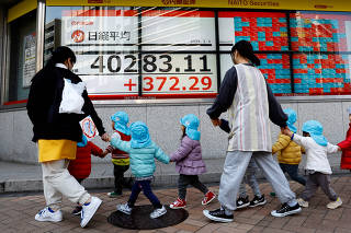 Children and their teachers walk past an electronic screen displaying Japan's Nikkei share average outside a brokerage in Tokyo