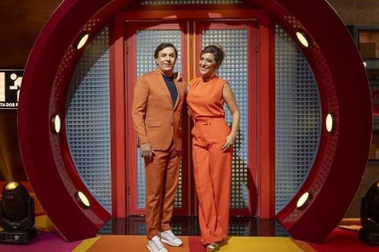 Em foto colorida, casal posa para foto em cima de um palco de um teatro