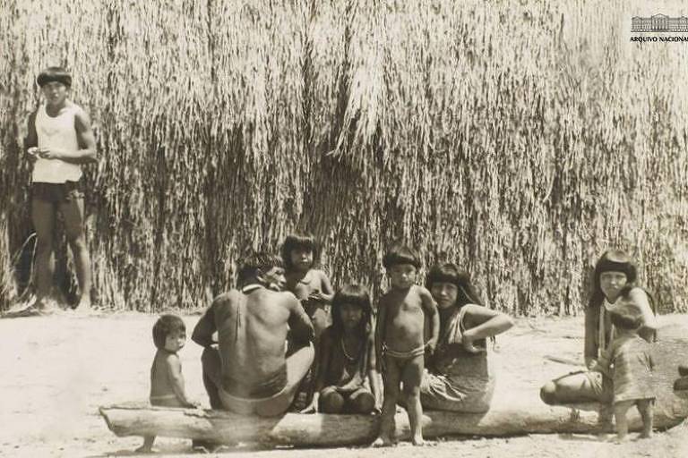 Indígenas reunidos, há crianças e adultos em foto preto e branco