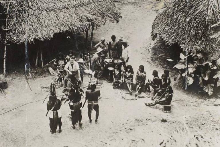 Indígenas reunidos próximos a ocas de palha