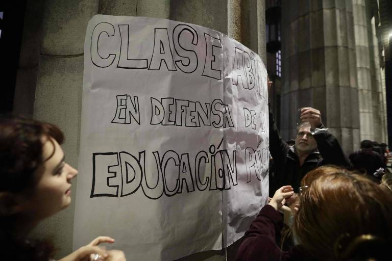 Estudantes colam cartaz em pilar da Faculdade de Direito da UBA, em Buenos Aires, com a frase 'aula aberta em defesa da educação pública', durante evento que debateu orçamento