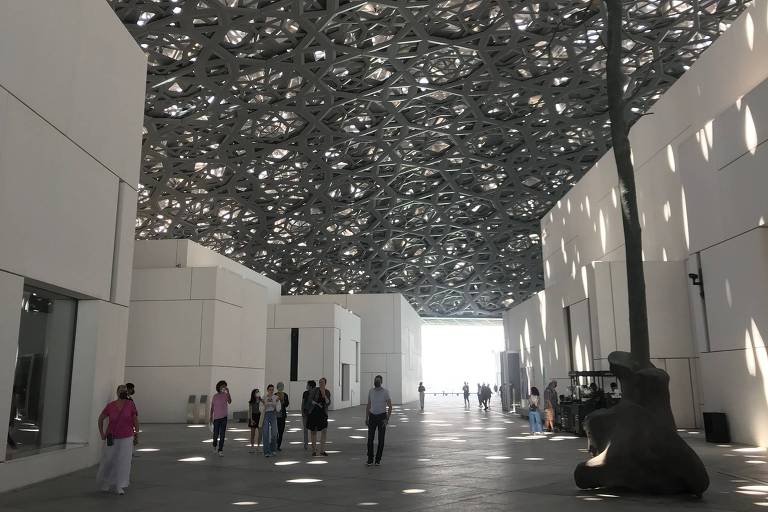 Pátio com teto de teias entrelaçadas e pessoas caminhando no Louvre de Abu Dhabi